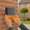 Hands installing a black and gold outdoor wall light on a brick wall. Produktbild-Vorschau