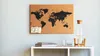 A cork world map pinboard hangs on a light blue wall above a white shelf with notebooks, glasses, and a water bottle. Produktbild-Vorschau