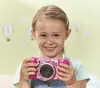 A young girl smiles while holding a pink VTech Kidizoom Duo Pro camera. Produktbild-Vorschau