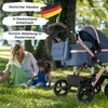 A woman and a child are sitting on the grass in a park next to a baby stroller. Produktbild-Vorschau