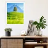A framed picture of a landscape with a tree and mountains hangs on a white wall above a wooden cabinet. The cabinet holds decorative items, including a plant, a clock, and a large letter 'A'. Anteprima dell’immagine prodotto