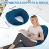 A woman is sitting on a bed, reading a book, and using a U-shaped pillow for support. The pillow is navy blue and has dimensions indicated. Produktbild-Vorschau