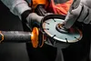 A person wearing gloves is holding an angle grinder and adjusting the blade. Voir les images du produit