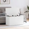 A white storage chest is open, placed next to a bed in a bedroom. A blanket is inside the chest. A lamp and a plant are visible in the background. Náhľad obrázku produktu