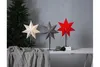 Three star-shaped lamps are displayed on a table in front of a Christmas tree and a gray wall. Podgląd zdjęcia produktu