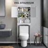 A bathroom scene featuring a toilet with an over-the-toilet storage cabinet filled with toiletries and towels. A sink and vanity are visible on the left, and a small stool with bottles is on the right. Náhled obrázku produktu