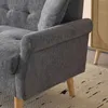 A close-up view of the armrest and side of a gray upholstered sofa, with wooden legs visible on a patterned rug. A wooden cabinet with a cane-style door is partially visible in the background. Produktbild-Vorschau