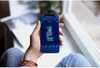 A person is holding a smartphone displaying a floor plan of a house, likely a smart home device app. Produktbild-Vorschau