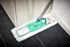 A mop is being used to clean a dark tiled floor next to a white cabinet and baseboard. Produktbild-Vorschau