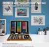 A wooden art set case is open, displaying various art supplies like markers, pencils, and pastels, set against a blue wall with framed artwork. Náhled obrázku produktu