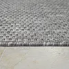 A close-up, low-angle shot of a gray woven rug with a textured pattern, resting on a light-colored tiled floor. Produktbild-Vorschau