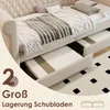 A beige sofa bed with two storage drawers pulled out, showing the mattresses inside. The bed is made with white and gray bedding and pillows. A patterned rug is visible on the floor. Voir les images du produit
