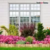A garden bed with pink flowers and green plants in front of a house window, bordered by a wooden fence. Náhled obrázku produktu