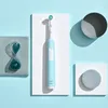 A light blue electric toothbrush is displayed on a white platform, with decorative elements like an hourglass and geometric shapes in gray and blue. Anteprima dell’immagine prodotto