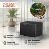 A black storage box is shown in a modern indoor/outdoor setting with a plant and a balcony scene in a circle. Produktbild-Vorschau