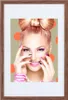 A woman with a bow-shaped hairstyle and vibrant makeup poses with her hands near her face, set against a backdrop of orange polka dots. Produktbild-Vorschau