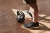 A person's legs and feet are shown standing next to a kettlebell on a wooden floor. Produktbild-Vorschau