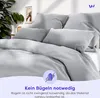 A neatly made bed with light gray bedding, featuring pillows and a duvet. Produktbild-Vorschau