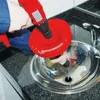 A person is using a red drain cleaning tool with a drill attachment in a stainless steel sink. Produktbild-Vorschau