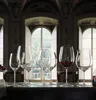 A collection of wine glasses filled with red wine and empty, arranged on a dark surface in front of large arched windows. Produktbild-Vorschau