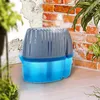 A blue and gray dehumidifier sits on a wooden surface next to a brick wall and plants. Produktbild-Vorschau