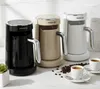 Three coffee makers in different colors (black, beige, white) are displayed on a marble countertop with coffee beans and cups. Produktbild-Vorschau