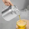 A hand is pouring oil from a stainless steel pitcher into a glass bowl. Podgląd zdjęcia produktu