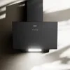 A black range hood mounted on a textured wall, with dramatic lighting and shadows. Voir les images du produit