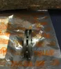 A close-up of a metal sprocket, likely for a chainsaw, is shown in its packaging. The background is dark and out of focus, with some text visible on the packaging. Produktbild-Vorschau