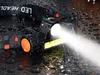 A black LED headlamp with an orange dial is shown in the rain, with water droplets on its surface and a bright beam of light emanating from it. Anteprima dell’immagine prodotto