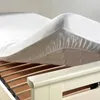 A white mattress protector is being placed onto a slatted bed base. Náhľad obrázku produktu