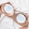A beige bra with disposable nursing pads placed inside the cups, lying on a white fluffy surface. Produktbild-Vorschau