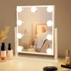 A makeup mirror with lights on a table, with makeup bottles and a brush in the foreground. Náhľad obrázku produktu