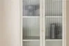 A close-up view of a beige vitrine with fluted glass doors, showcasing decorative vases inside. Voir les images du produit