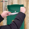 A person is putting mail into a green mailbox mounted on a wooden wall. Anteprima dell’immagine prodotto