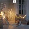 A child sits on a cloud-shaped rug in a nursery, holding a teddy bear, with a crib and a decorative light tree in the background. Podgląd zdjęcia produktu