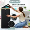 A woman is interacting with a black laundry basket next to a washing machine in a laundry room. Produktbild-Vorschau