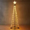 A cone-shaped Christmas tree decorated with warm white LED lights and a star on top, standing on a wooden floor against a concrete wall. Podgląd zdjęcia produktu