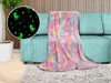 A glow-in-the-dark unicorn blanket is draped over a teal sofa in a living room setting. Náhľad obrázku produktu