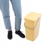 A person's legs and feet are shown next to a yellow trash can. Produktbild-Vorschau
