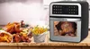An air fryer is shown next to a table with various cooked foods, including a whole roasted chicken, chicken wings, and french fries. Produktbild-Vorschau