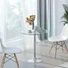 A round glass-top dining table with a silver metal base, set with two cups of coffee, a teapot, and a vase of flowers. Two white chairs are positioned on either side of the table, in a room with sheer white curtains and a green ombre curtain in the backgro Produktbild-Vorschau