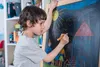 A young boy is drawing on a blackboard with chalk. Anteprima dell’immagine prodotto