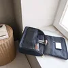 An open navy blue toiletry bag with makeup brushes and a compact inside, resting on a marble surface next to a woven basket. Anteprima dell’immagine prodotto