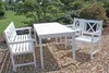 A white wooden table and bench set in a garden setting with wood chips on the ground. Produktbild-Vorschau