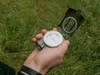 A hand holding an open compass over grass. Podgląd zdjęcia produktu
