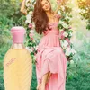 A woman sits on a floral swing in a garden, with a perfume bottle in the foreground. Anteprima dell’immagine prodotto