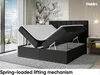 A bed with its storage compartment open, showcasing the lifting mechanism. Produktbild-Vorschau
