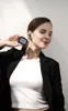 A woman is holding a pair of black wireless earbuds and their charging case, with one earbud in her ear. Voir les images du produit