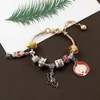 A charm bracelet with various Halloween-themed charms is laid out on a brown surface with a green leaf illustration in the background. Produktbild-Vorschau